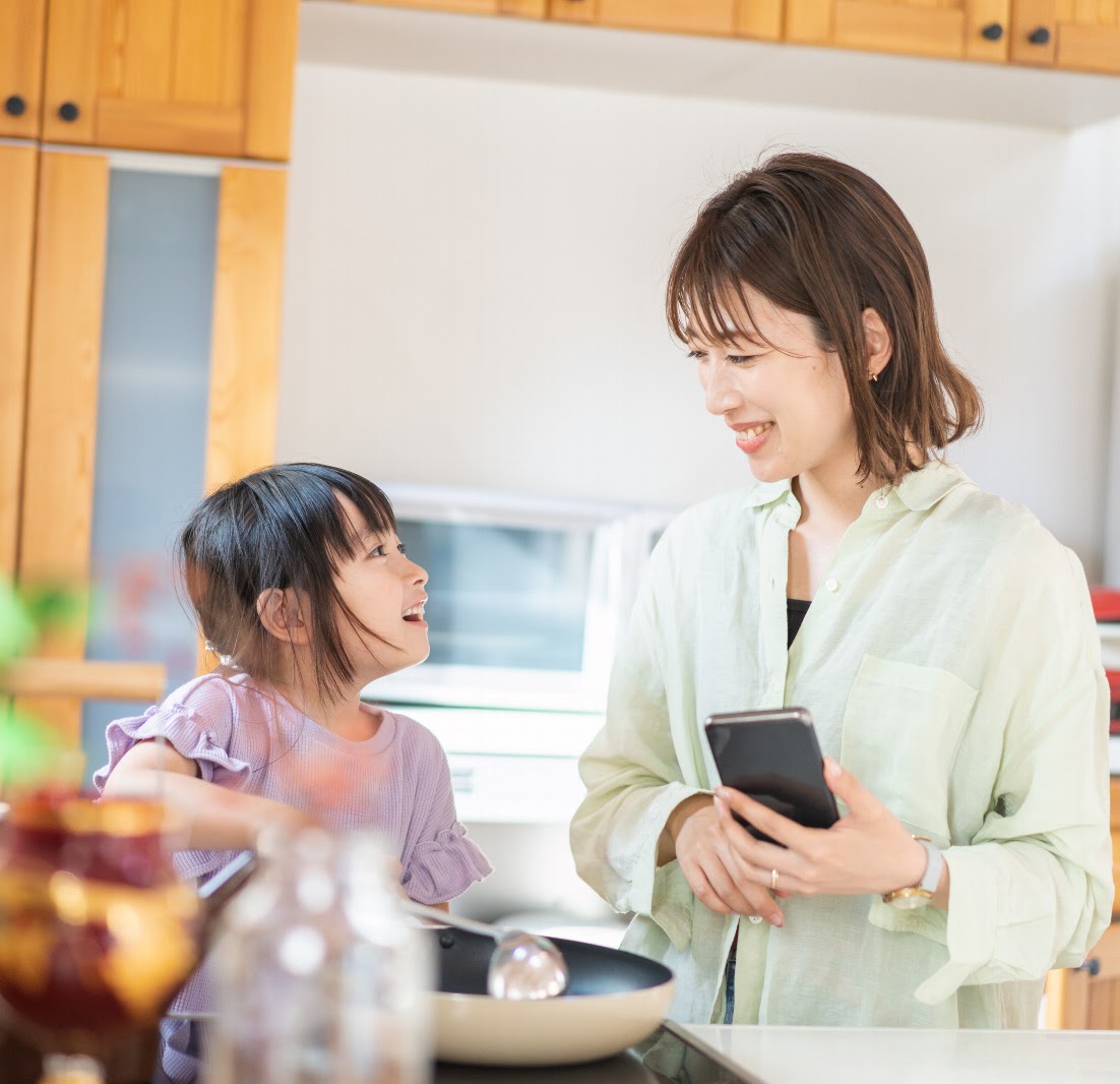 キッチンでスマートフォンを見ながら料理を楽しむ親子